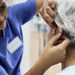 An audiologist fitting a woman with a new hearing aid.