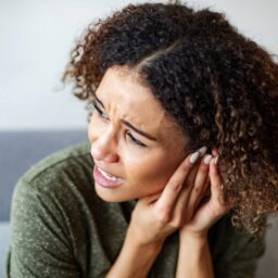 A woman experiencing ear pain holds her hands to her left ear.