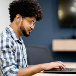 Man wearing hearing aids working on laptop at office