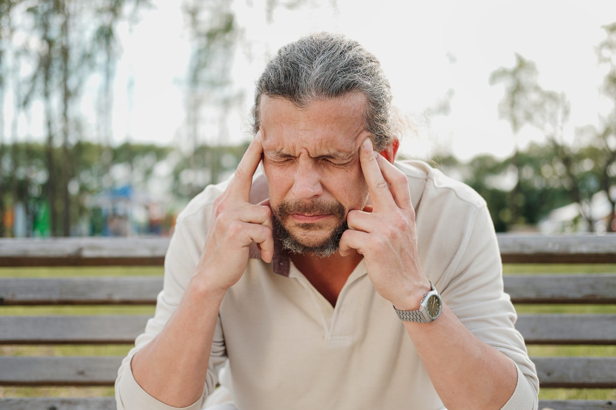 man on bench holding temples in visible pain