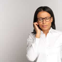 Woman experiencing pulsatile tinnitus holding her ear and looking uncomfortable.