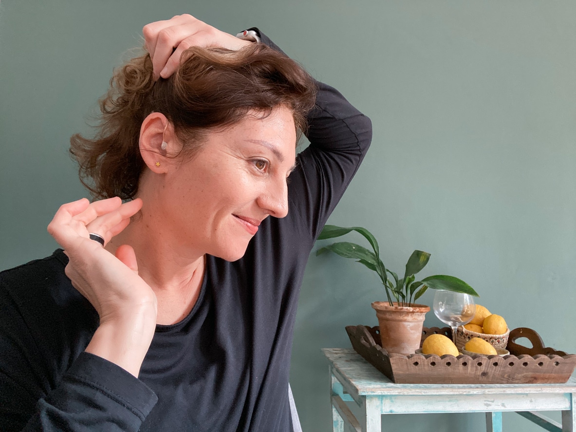 A woman adjusts her hearing aid into the correct position confidently.