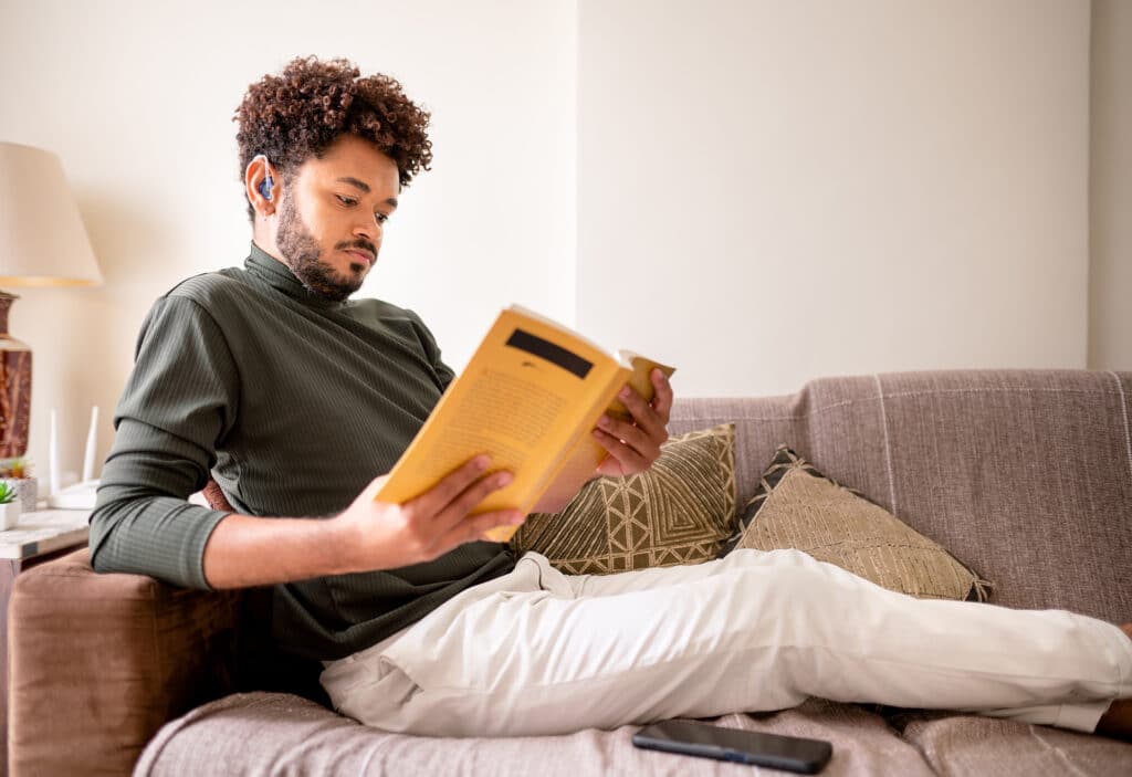 Man with hearing aids listening to an audiobook and reading the physical book
