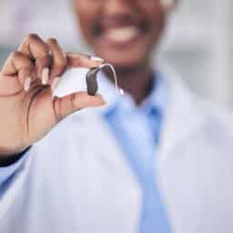 Smiling audiologist holds up a new top-of-the-line hearing aid