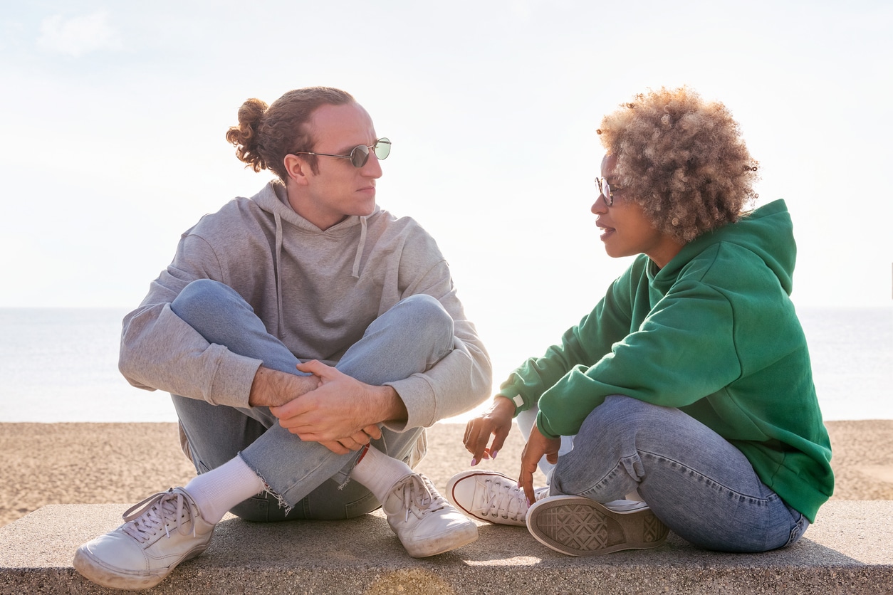 Two people sitting on a sunny beach chatting