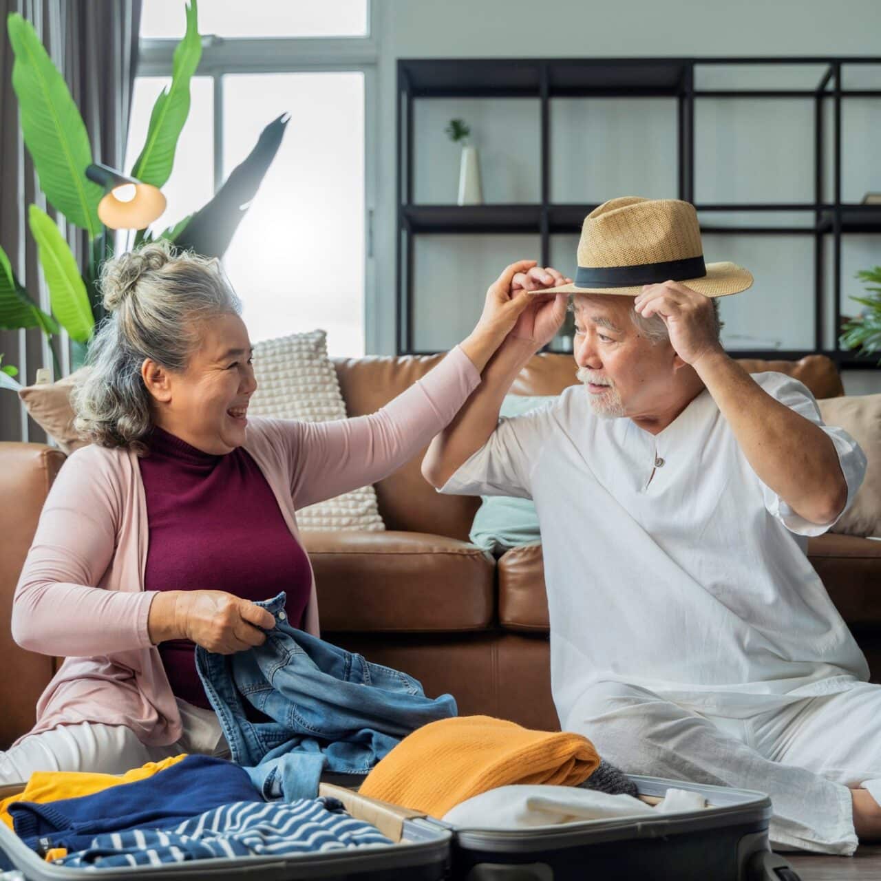 Older man playfully trying on a hat while his spouse laughs