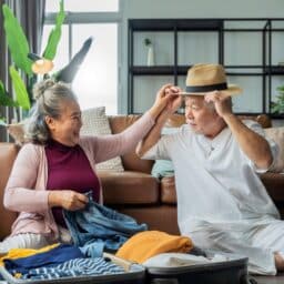 Older man playfully trying on a hat while his spouse laughs