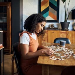 Woman doing a jigsaw puzzle to stay sharp on the dining room table in a trendy home.