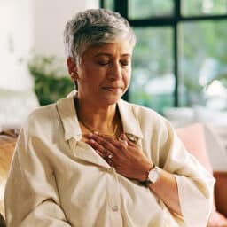 Woman with hypertension holding her chest and breathing deeply to manage high blood pressure and chest pain.