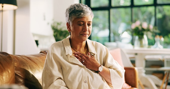Woman with hypertension holding her chest and breathing deeply to manage high blood pressure and chest pain.